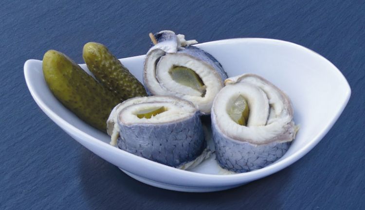 Rollmops mit Gewürzgurken in weißer Schale auf blauem Hintergrund