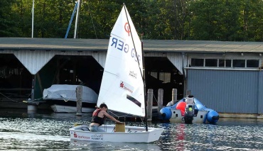 Junge im Segelboot vor Bootsschuppen