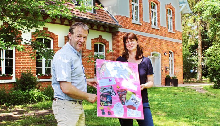 Bildübergabe Sozius Schwerin Andreas Scher und Mitarbeiterin von Sozius Schwerin bei der Übergabe des gebastelten Bildes vor dem Soziusgebäude